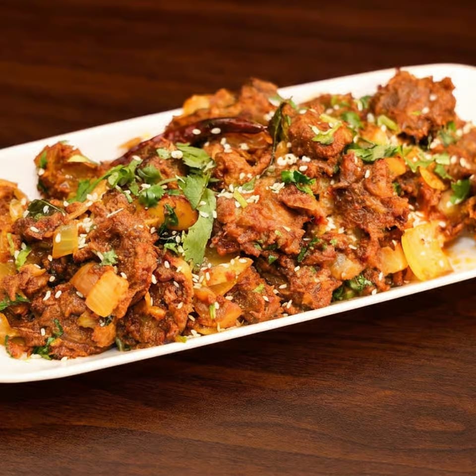 Crispy spiced vegetable fritters garnished with cilantro and sesame seeds on a white rectangular platter.