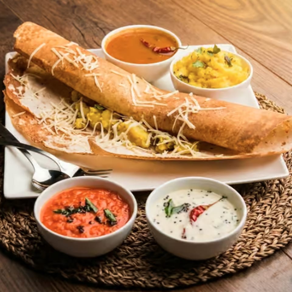 Stuffed toasted flatbread with shredded cheese and vegetables, served with four bowls of colorful sauces on a woven placemat.