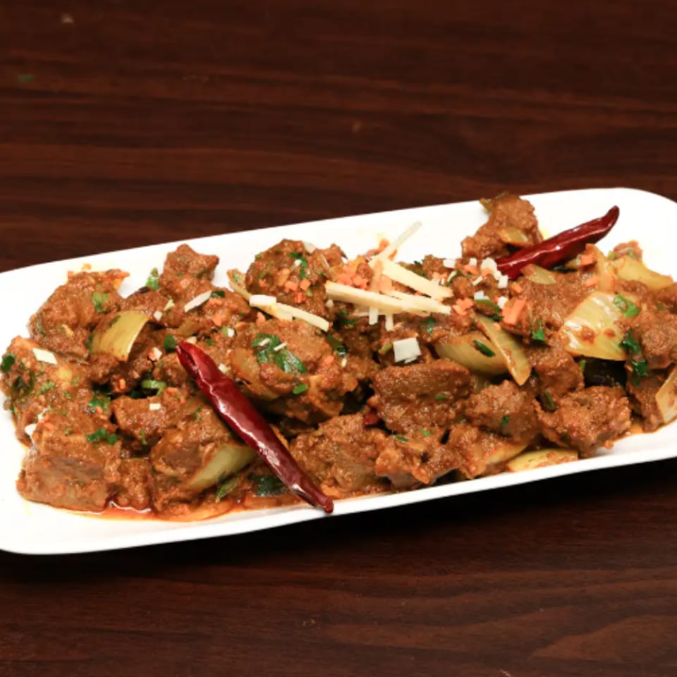 Spicy minced meat dish garnished with dried red chilies, herbs, onions, and sliced vegetables on a white platter.