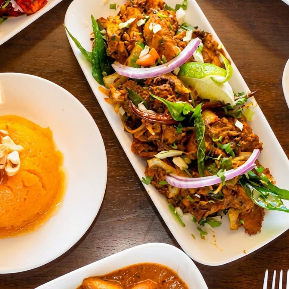 A top-down view of various Indian dishes, including chicken curry, a dessert, and a fried appetizer.