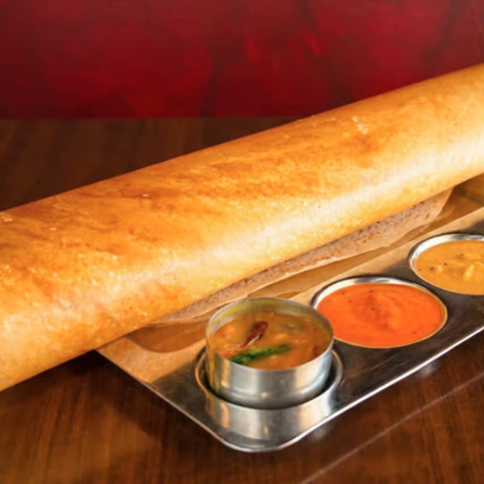 Golden dosa served with four colorful chutneys on a metal tray atop a wooden table.